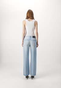 Vaaleansiniset leveälahkeiset farkut, joissa kulunut pinta, takataskut ja musta merkki. Yhdistetty valkoiseen hihattomaan toppiin, nähtynä takaa.