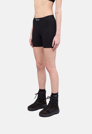Pantalones cortos negros con canalé y una cinturilla gruesa que presenta una marca blanca, combinados con botas negras hasta el tobillo y calcetines. Textura mate suave.