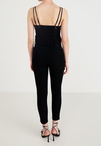 Černý zkrácený top s nařasenými detaily a nastavovacími ramínky, v kombinaci s úzkými černými kalhotami a páskovými vysokými podpatky s ozdobami.