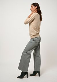 Maglione beige lavorato a maglia con scollo rotondo, texture morbida, abbinato a jeans grigi a gamba larga con orli sfrangiati e stivaletti neri con tacco alto.