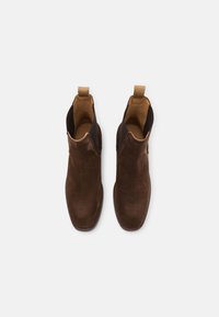 Bottines en suede marron avec panneaux élastiques sur les côtés et une languette, présentant une texture lisse et une forme de bout arrondi.