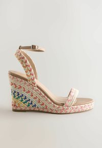 Sandale compensée beige avec bride à la cheville, bout ouvert et détail tressé multicolore enveloppant le talon compensé et le bord de la semelle.