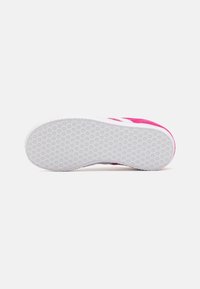 Vaaleanpunainen mokkanahkainen tennarin pohja, jossa valkoinen kumipohja teksturoidulla, pyöreällä kuvioinnilla pitävyyttä varten ja kantapään myötäisellä kaarevalla muotoilulla.