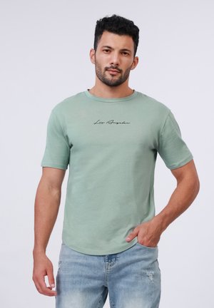 Mintgrøn kortærmet t-shirt med rund hals og sort "Los Angeles" tekst. Stoffet ser blødt ud med en let struktur. Båret med lyseblå jeans.