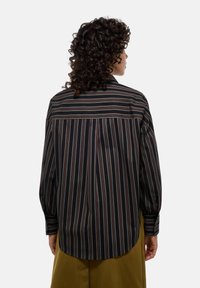 Chemise rayée aux couleurs noir, crème et bordeaux. Manches longues avec des poignets à boutons, ourlet incurvé et détails de découpe au dos. Tissu au toucher lisse.