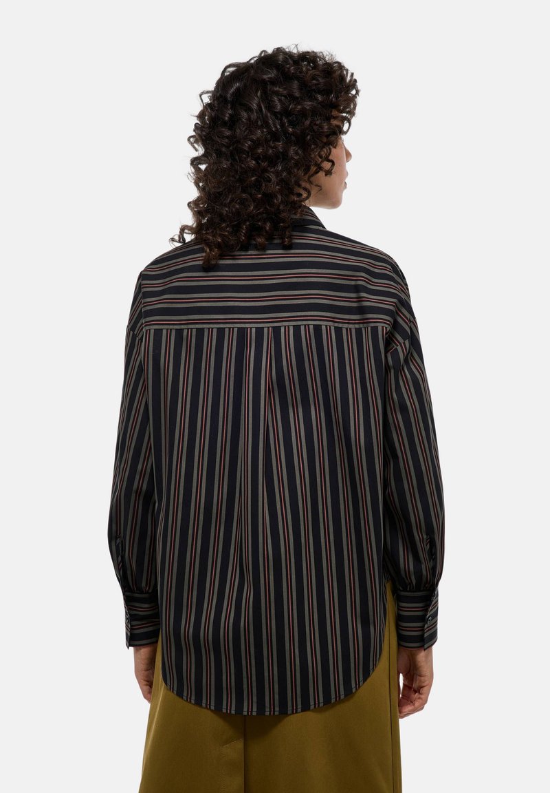 Chemise rayée aux couleurs noir, crème et bordeaux. Manches longues avec des poignets à boutons, ourlet incurvé et détails de découpe au dos. Tissu au toucher lisse.
