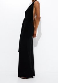 Robe maxi noire sans manches, avec un design portefeuille et un dos ouvert, fabriquée en tissu doux à la texture lisse et à la silhouette ajustée.