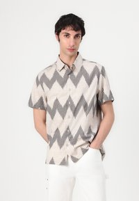 Kortefsleevenshirt in lichtbeige met zwart zigzagpatroon en knopenfront. Gemaakt van textuurstof, dat hedendaags ontwerp met comfort combineert.