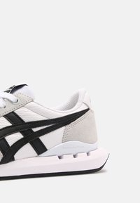 Light grey and white sneaker featuring black stripes, a textured leather upper, and a cushioned sole with a distinctive logo on the heel.