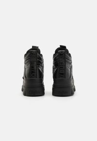 Sneaker alte nere con texture trapuntata, colletto imbottito e etichetta prominente sul retro. Suola in gomma spessa per un'altezza extra.
