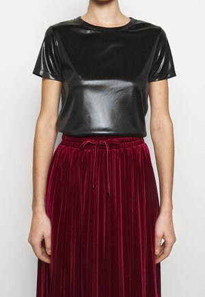 Žena má na sobě krátký lesklý černý top v kombinaci s vysoce pasem, plisovanou burgundskou sametovou sukní se stahovací šňůrkou v pase.