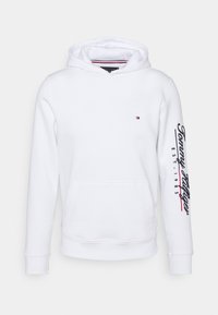 Sudadera blanca con un bolsillo frontal tipo pouch, capucha ajustable con cordón y texto impreso en rojo y azul marino en la manga izquierda.
