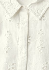 Vit skjorta med en texturerad bomullstyg och broderade blommönster samt utskurna detaljer. Klassisk krage och knappstängning fram.