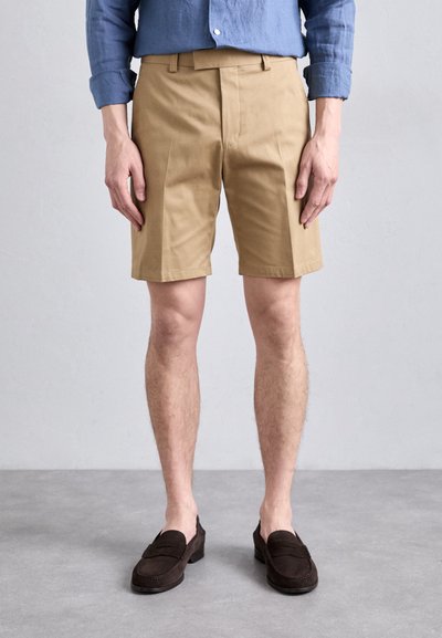 Khaki katoenen shorts met een rechte snit, voorzien van voorplooien, riemlusjes en een gladde textuur, gecombineerd met donkerbruine instappers.