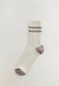 Krém színű zokni vízszintes barna csíkokkal, bordázott textúrával, kerek orral és megerősített sarokrésszel.
