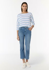 Gestreiftes blaues und weißes Langarmhemd kombiniert mit hellblauen, geraden Jeans und weißen Sneakers. Minimalistisches Design, lässiger Schnitt.