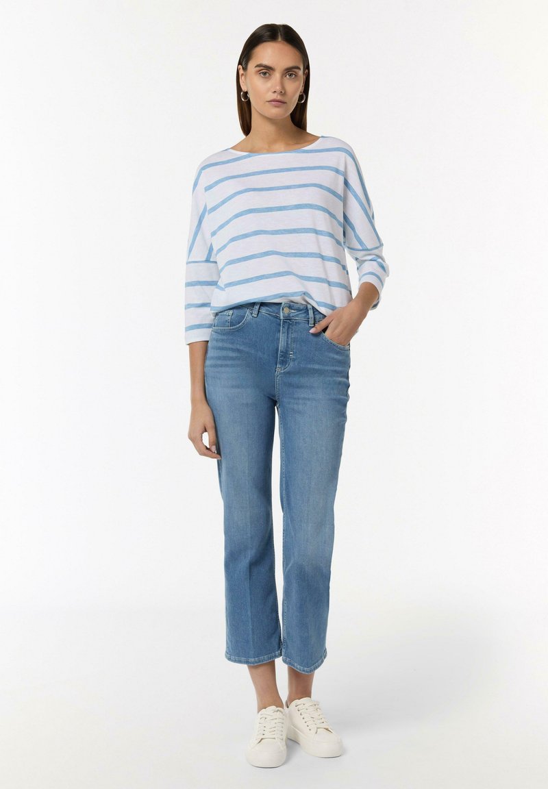 Gestreiftes blaues und weißes Langarmhemd kombiniert mit hellblauen, geraden Jeans und weißen Sneakers. Minimalistisches Design, lässiger Schnitt.