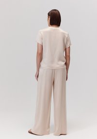 Beżowa satynowa bluzka z krótkimi rękawami i okrągłym dekoltem, w połączeniu z spodniami z wysokim stanem i szerokimi nogawkami w pasującym jasnym odcieniu.