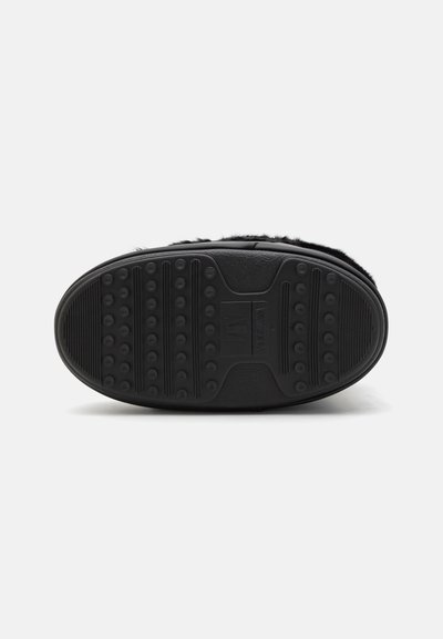 Semelle de chaussure noire en caoutchouc texturé, avec des crampons circulaires et striés pour une meilleure adhérence. Dessus doux et pelucheux partiellement visible le long du bord.