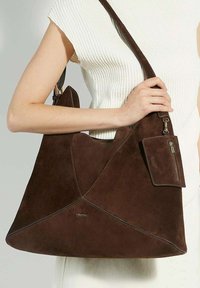 Brown suede tote bag with angular design and a detachable zippered pouch. Features a single shoulder strap and embossed brand logo.
