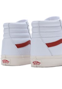 Vita läder höga sneakers med röda accenter på sidan, med en texturerad yta och en Vans logo patch på hälen.