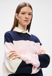 Μπλούζα πόλο σε ναυτικό μπλε, ροζ και κρέμα. Διαθέτει γιακά, λεπτομέρειες από λάδι και μανίκια με χρωματική μπλοκ εκτύπωση και μαλακή υφή.