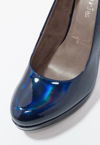 Gros plan sur une chaussure en cuir verni bleu foncé brillant avec un bout arrondi et une doublure intérieure beige douce.