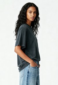 Tricou cu mânecă scurtă, de culoare gri închis, cu un croi lejer și gât rotund, asortat cu blugi din denim albastru deschis, cu talie înaltă și buzunare.