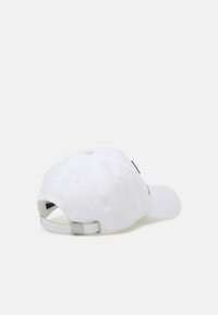 Hvit bomullsbasketcap med buet skjerm, justerbar metallbeslag og brodert detalj på siden. Glatt tekstur, minimalistisk design.