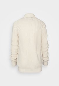 Béžový pletený svetr s žebrovanou strukturou. Má složený límec a dlouhé rukávy, s mírně volným střihem a spodním lemem.