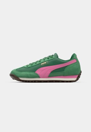 Groene suède sneakers met roze accenten, uitgerust met een rubberen zool en vetersluiting. Gouden tekst met "Puma Easy Rider" aan de zijkant.