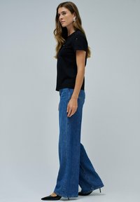Top negro de manga corta con detalles bordados, combinado con vaqueros de tiro alto de pierna ancha azules y tacones negros de punta.
