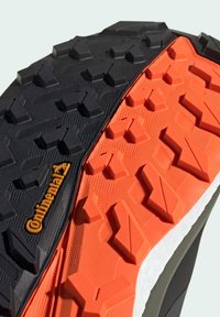Trail løbesko sål med et sort og orange design. Robust gummimateriale med et struktureret mønster for forbedret greb.