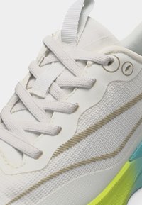 Λευκό αθλητικό παπούτσι με υφή υφάσματος, λευκά κορδόνια και ενδιάμεση σόλα με μπλε και νέον κίτρινα διακοσμητικά στοιχεία.