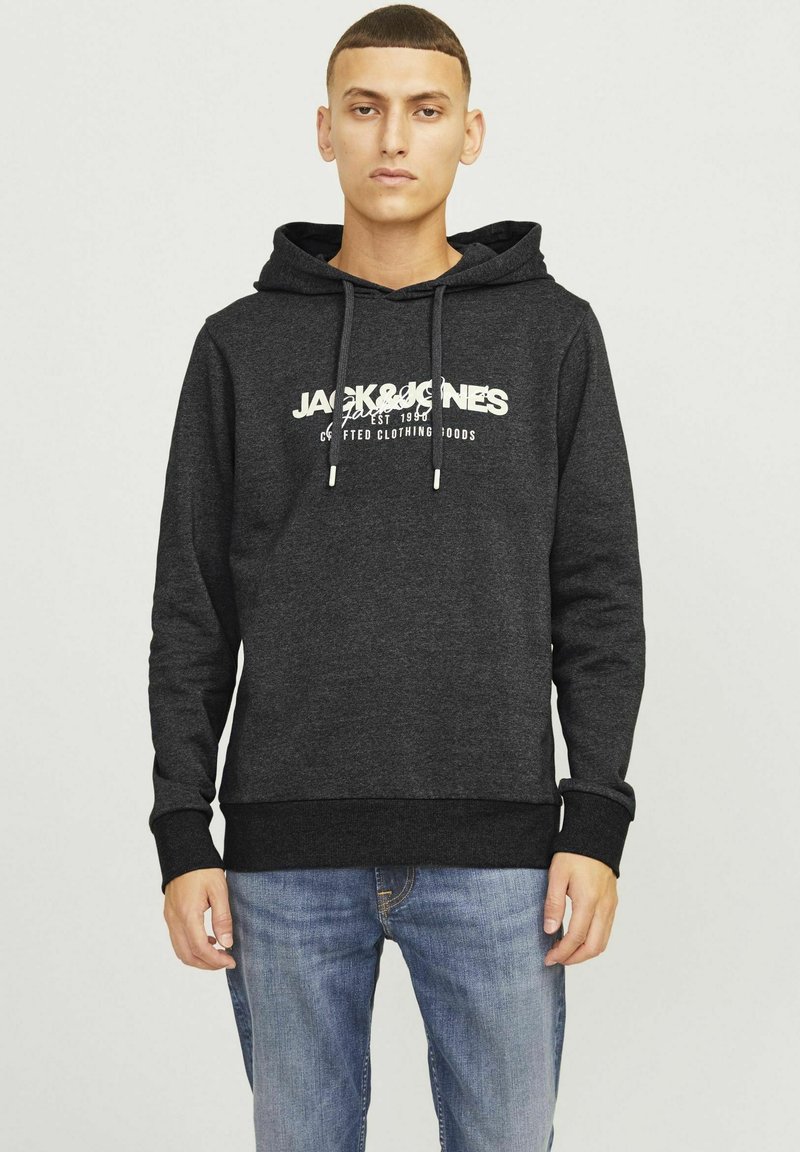 Grijze hoodie met een groot wit logo en tekst op de voorkant, met een trekkoord en een kangoeroezak. Gecombineerd met blauwe spijkerbroek.