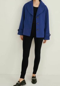 Blå oversized jacka i ullblandning med stora slag, tre knappar och manschettdetaljer, kombinerad med svarta åtsittande leggings och svarta loafers.