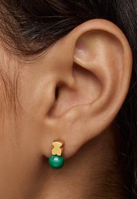 Pendientes de oro y verde con un pendiente en forma de oso y una esfera de malaquita. Textura suave con colores y formas contrastantes.