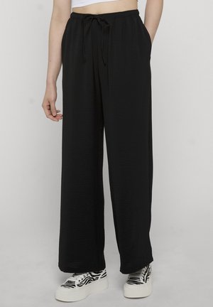 Person som har på seg svarte vide bukser med snor i midjen og hvite platåsneakers med svarte zebrastriper.