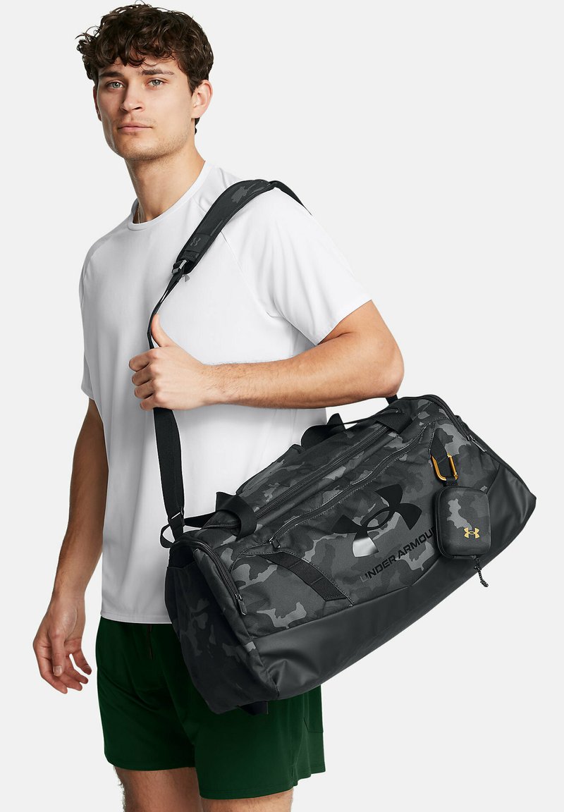 Schwarze Tarn-Duffle-Tasche mit mehreren Fächern, strapazierfähigem Material, zwei Griffen, verstellbarem Schultergurt und einem markierten Reißverschlussbeutel.