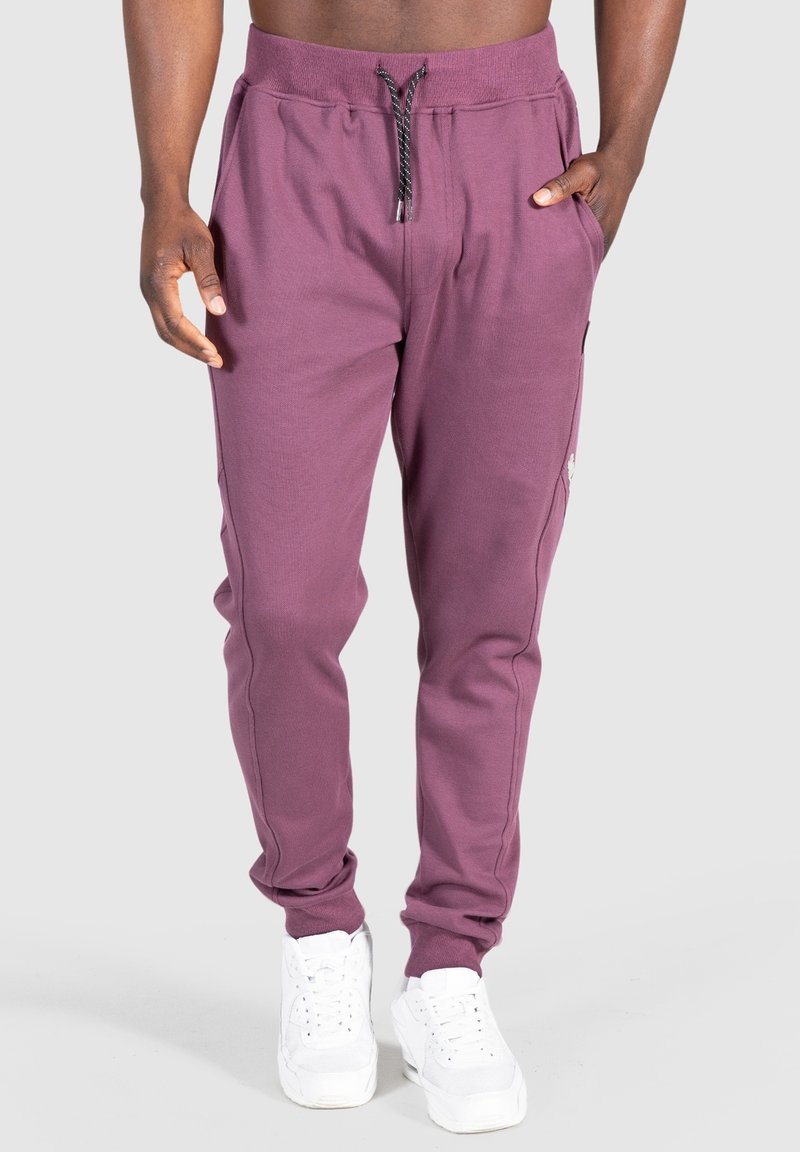 Pantalones jogger de algodón morados con cintura elástica, cordón ajustable, bolsillos laterales y tobillos con puños, combinados con zapatillas blancas.