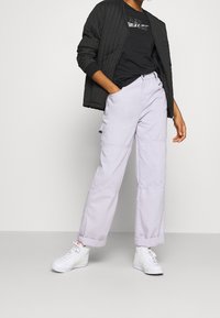 Ljust lavendelfärgade vida cargobyxor med sydda paneler, matchade med en svart vadderad bomberjacka och vita sneakers.