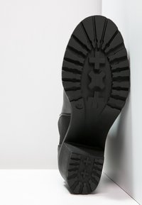 Czarna gumowa podeszwa buta z teksturowanym wzorem bieżnika z charakterystycznymi krzyżykami, zapewniającymi przyczepność. Gładka krawędź zewnętrzna, z lekko podniesionym obcasem i widocznym oznaczeniem rozmiaru.