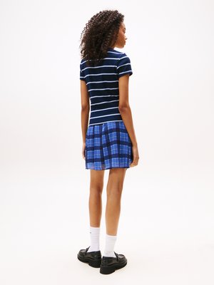 Haut rayé bleu marine à manches courtes associé à une jupe à carreaux bleus, présentant différentes nuances. Chaussures à plateforme noires, chaussettes blanches montantes.