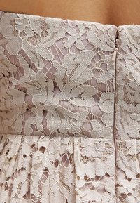 Lace dress featuring intricate floral patterns in light beige, with a zipper closure on the side and pleated skirt detailing.