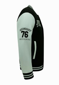 Zwart-witte varsityjas met geborduurd "NEW YORK" en "MIDNIGHT 76 AUTHENTIC." Voorzien van gestreepte boorden en zakken. Glad textuur.