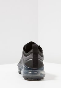 Scarpa sportiva nera con tomaia testurizzata, suola con ammortizzazione ad aria traslucida e linguetta sul retro. Presenta il marchio "Vapormax".