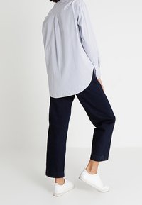 Blue and white striped button-up shirt with a curved hem, paired with dark blue, loose-fitting trousers and white sneakers.