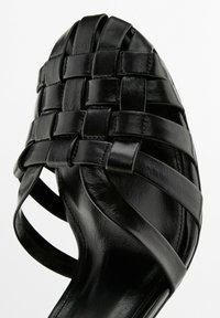 Sandal in pelle intrecciata nera con un design incrociato sulla punta, dotata di cinturini piatti e una finitura liscia. Apertura sul retro per favorire la traspirabilità.