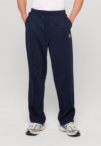 Granatowe spodnie dresowe z miękkiego materiału, z regulowanym paskiem w talii, bocznymi kieszeniami oraz haftowanym logo na lewym udzie.