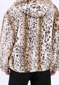 Faux fur jakke i tan og creme med leopardmønster, der har hætte og ribbet kant. Blød tekstur og løstsiddende design.